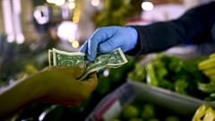  Owner of a fruit and vegetables stand, wears gloves as he exchanges cash with a customer