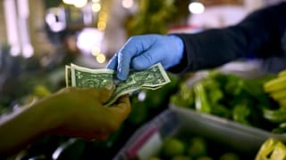  Owner of a fruit and vegetables stand, wears gloves as he exchanges cash with a customer