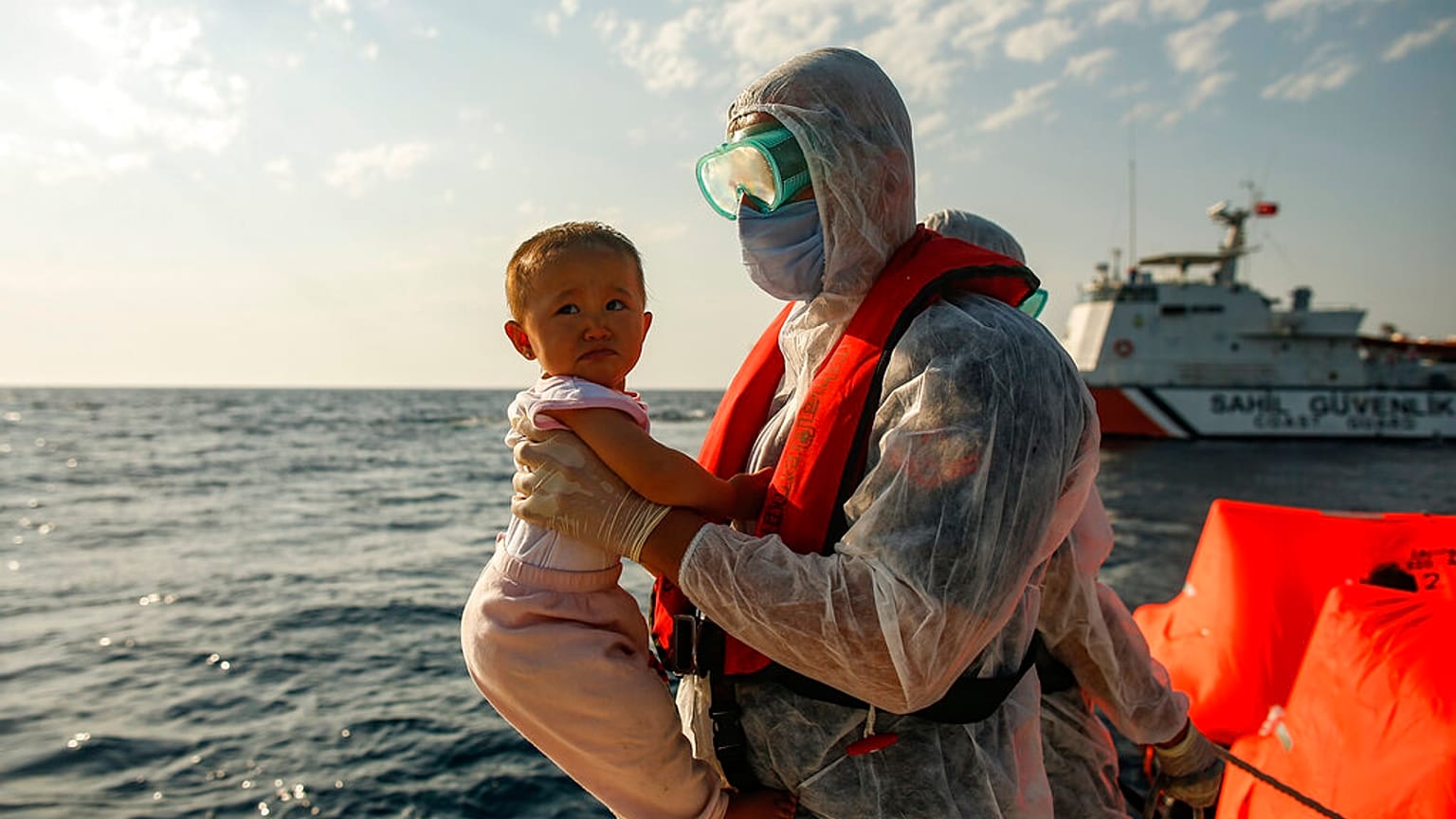 A Turkish coast guard officer, wearing protective gear to help prevent the spread of coronavirus, carries a child off a life raft during a rescue operation in the Aegean Sea, 