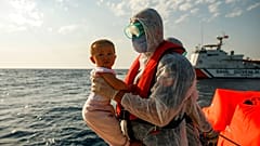 A Turkish coast guard officer, wearing protective gear to help prevent the spread of coronavirus, carries a child off a life raft during a rescue operation in the Aegean Sea, 
