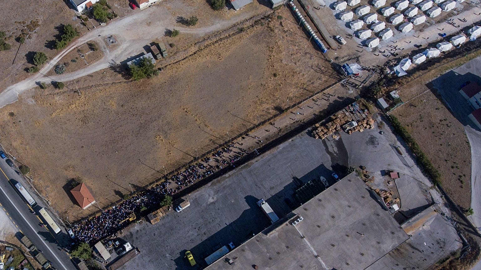 FILE - Migrants wait to depart from Lesbos for mainland Greece outside a temporary refugee camp in Kara Tepe.