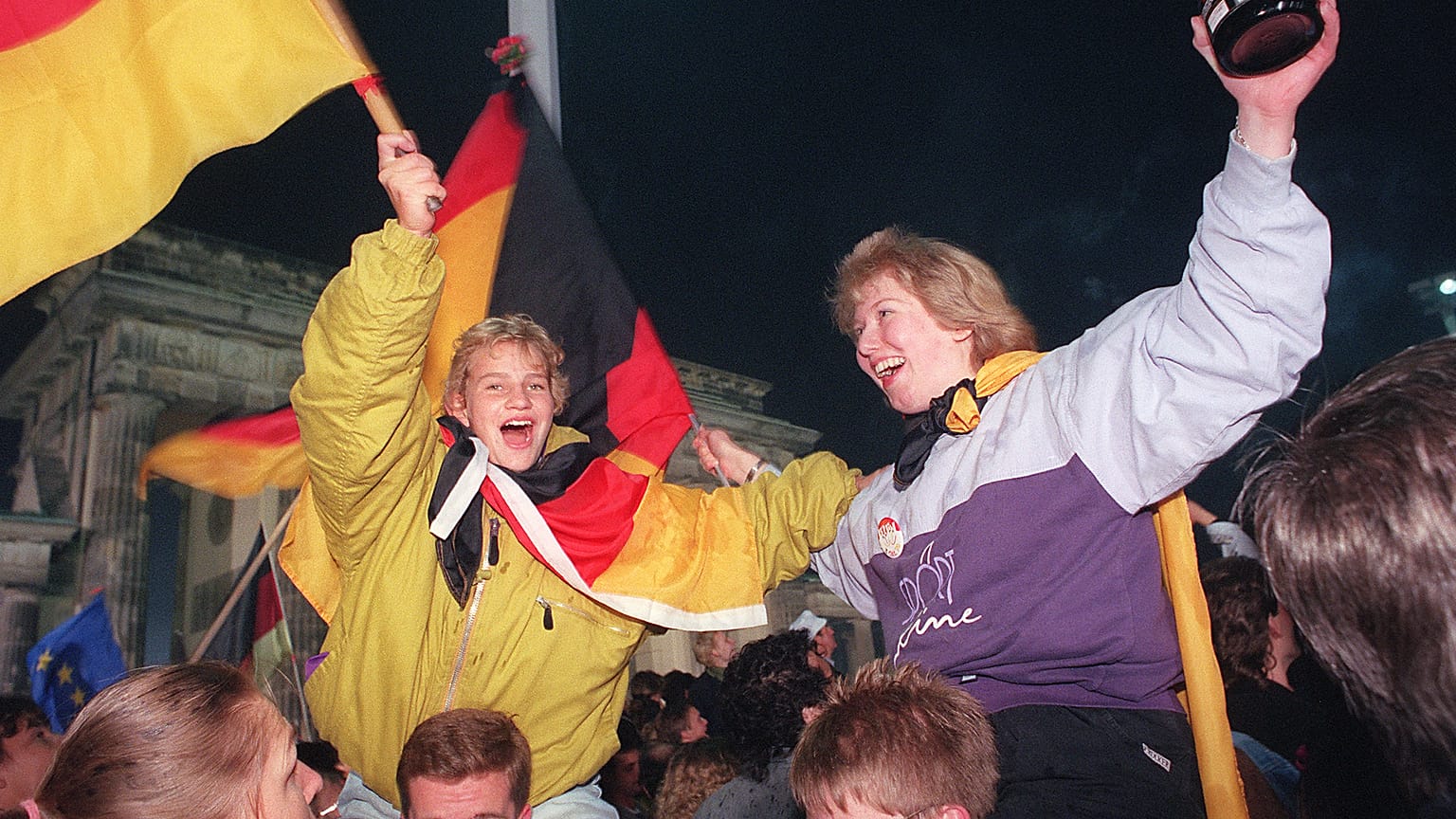 Jóvenes berlinesas ondean banderas alemanas durante la celebración de la reunificación del país en la Puerta de Brandenburgo, Berlín. 3 de octubre de 1990