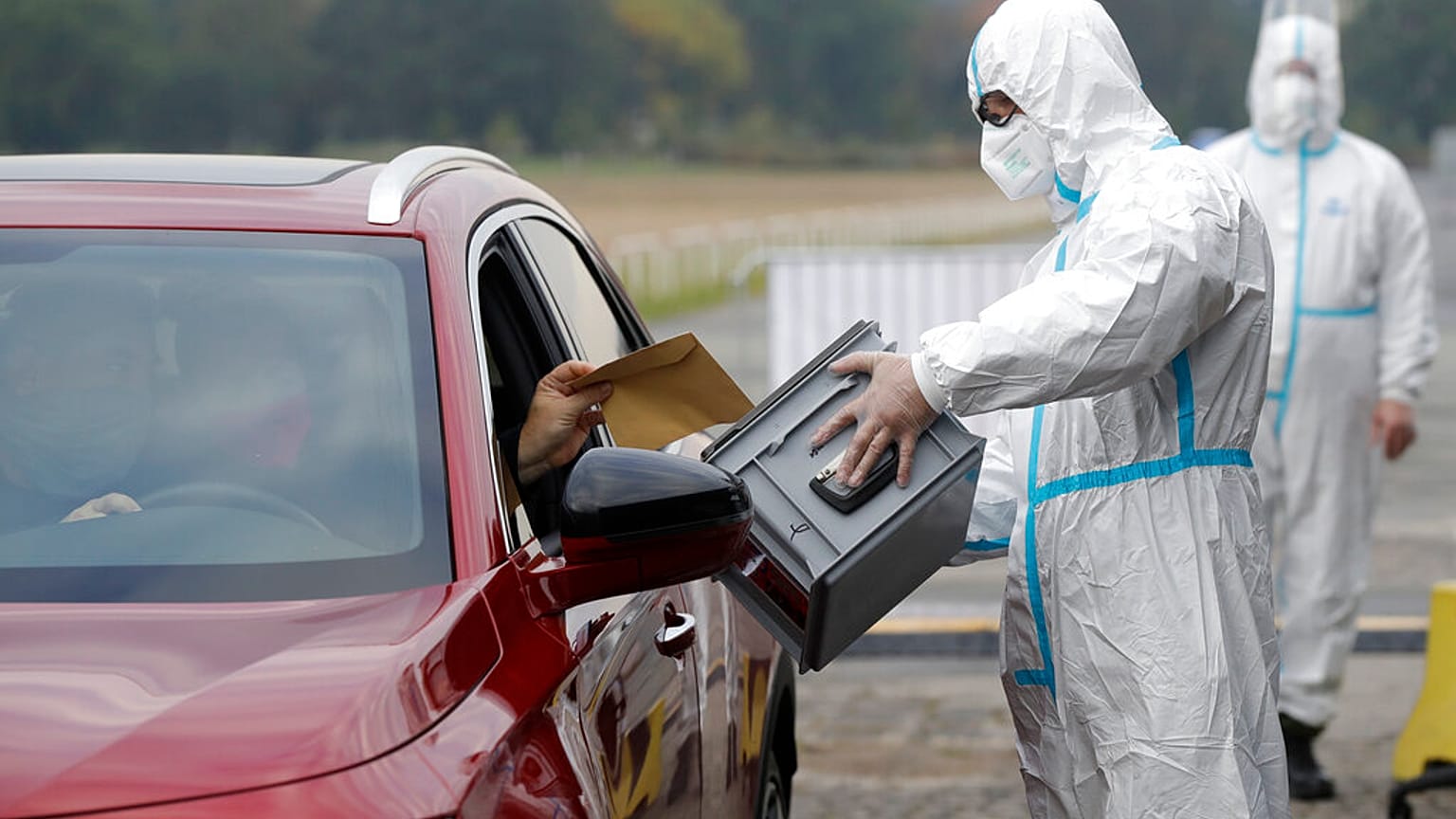 An election committee member, wearing a protective suit, holds a ballot box for a man to vote in regional and senate elections at a drive-in polling station in Prague.