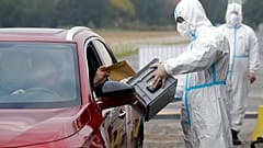 An election committee member, wearing a protective suit, holds a ballot box for a man to vote in regional and senate elections at a drive-in polling station in Prague.