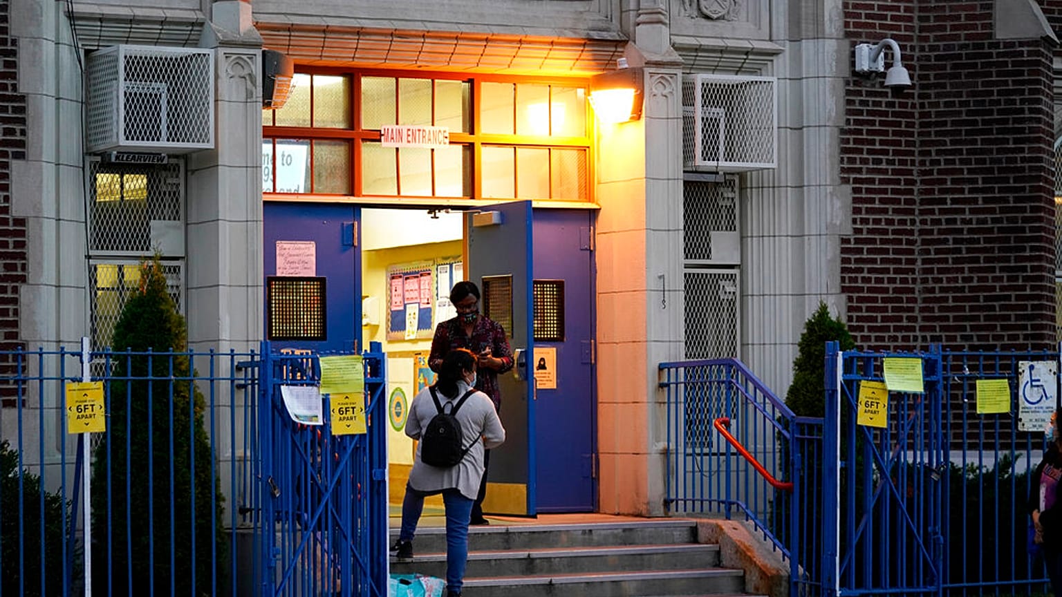 A Department of Education employee talks to a parent on the steps outside Public School 95 in Brooklyn's Gravesend neighborhood Monday, Oct. 5, 2020, in New York.
