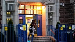 A Department of Education employee talks to a parent on the steps outside Public School 95 in Brooklyn's Gravesend neighborhood Monday, Oct. 5, 2020, in New York.