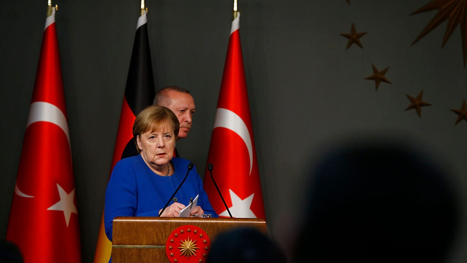 Germany's Chancellor Angela Merkel, left, stands as Turkey's President Recep Tayyip Erdogan, walks behind her 