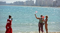 زوار يحملون الأعلام التركية المنفصلة يلتقطون صورًا لبعضهم البعض على الشاطئ مع المباني المهجورة بعد أن فتحت الشرطة شاطئ فاروشا.