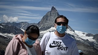 Touristen mit Mundschutz vor dem Matterhorn. 