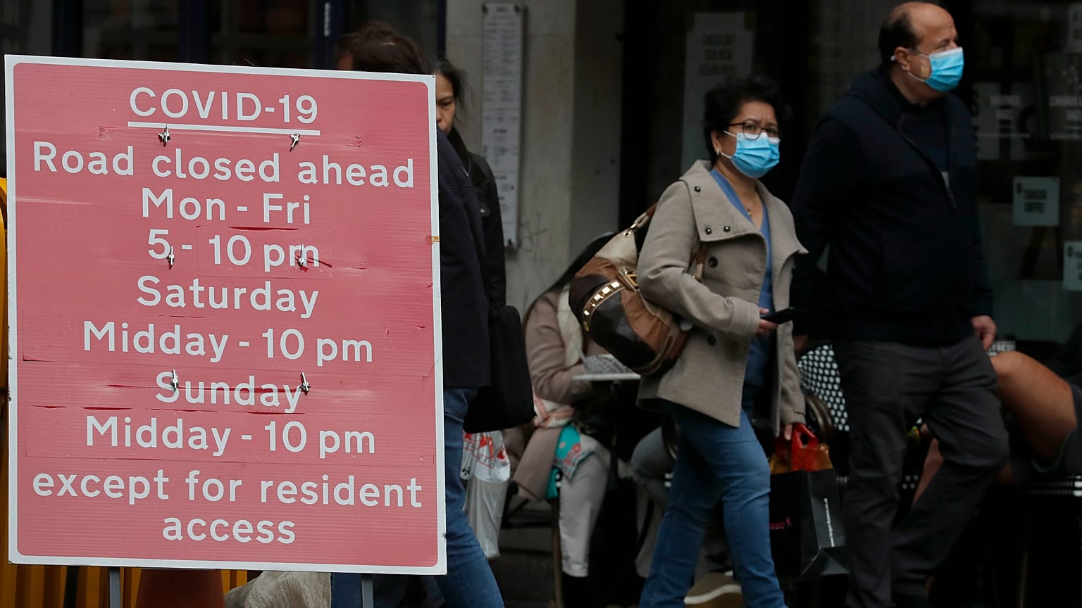 People walk past a sign that refers to COVID-19 closures in London, Friday, Oct. 9, 2020.