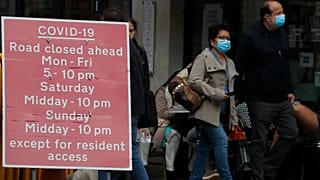 People walk past a sign that refers to COVID-19 closures in London, Friday, Oct. 9, 2020.