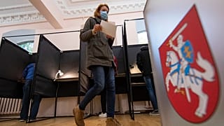 A voter walks past the Lithuanian coat of arms at a polling station during parliamentary elections in Vilnius, Lithuania, Sunday, Oct.11, 2020. 