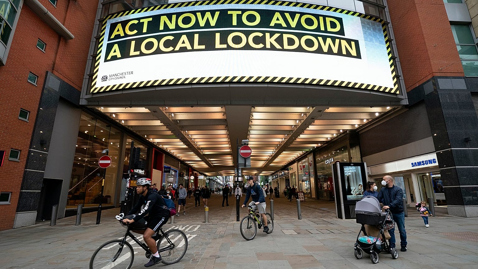 Members of the public pass a public information message in central Manchester.