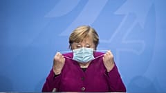 German Chancellor Angela Merkel holds her face mask as she arrives for a press conference after a meeting with the governors of the German states in Berlin, Oct. 14, 2020.