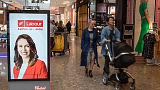 Jacinda Ardern munkáspárti politikus plakátja mellett halad egy pár egy Christchurch-i bevásárlóközpontban