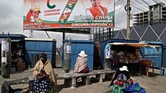 A billboard promoting presidential candidate Carlos Mesa of the Citizen Community political party towers over a trio of women in Rio Seco, Bolivia, Saturday, Oct. 17, 2020