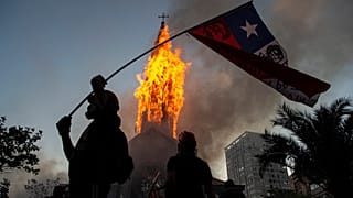 Un manifestante enarbola una bandera de Chile frente a la cúpula de la Asunción en llamas