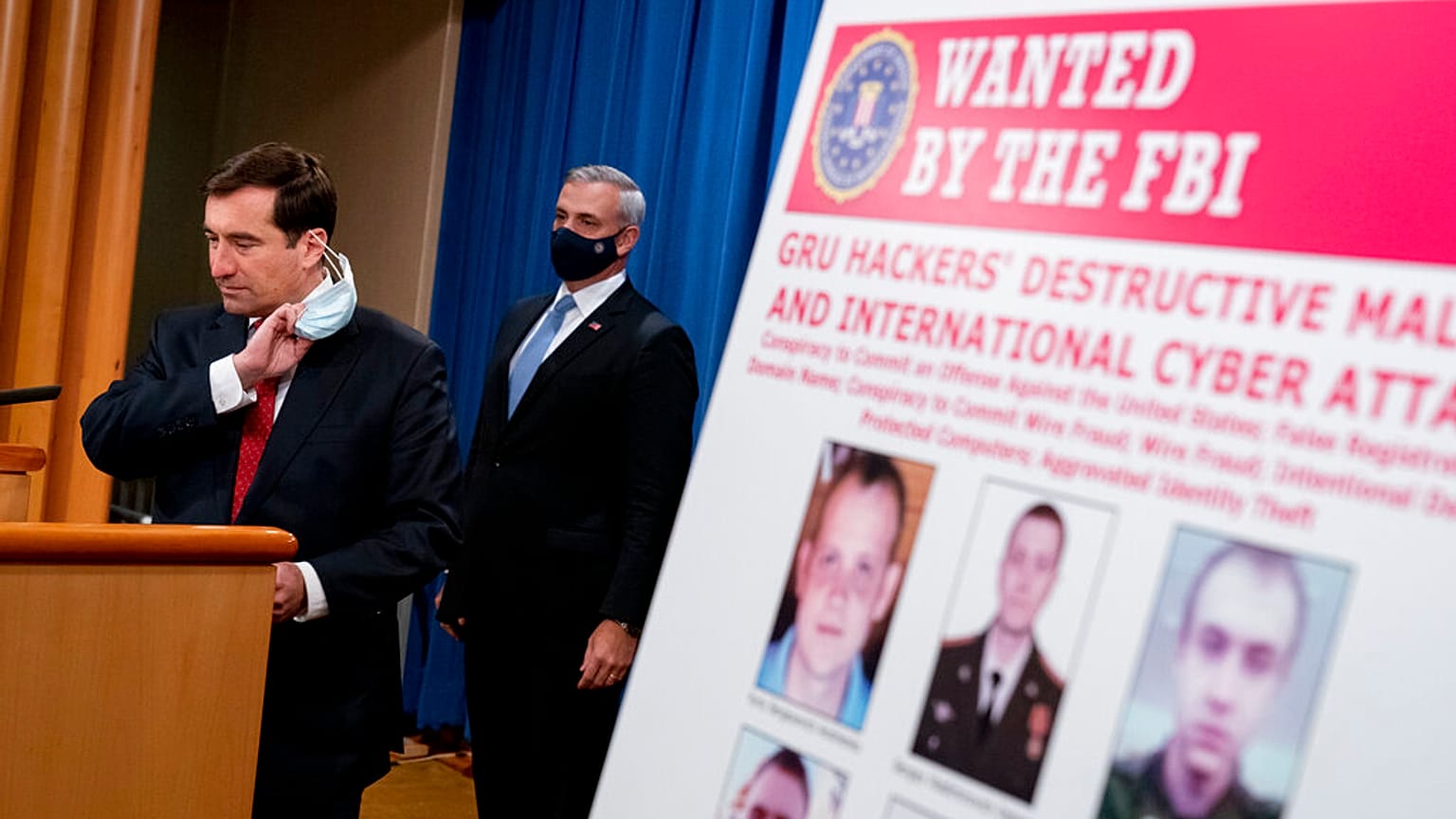 A poster showing six wanted Russian military intelligence officers is displayed as Assistant Attorney General for the National Security Division John Demers, speaks.