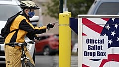 Cyclist Mickey McDiarmid votes by dropping her completed ballot into a ballot drop box Monday, Oct. 19, 2020, in Bellingham, Washington.