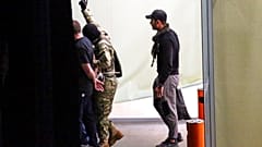 O δράστης αποχωρεί από την τράπεζα με τρεις ομήρους και έναν αστυνομικό να τον ακολουθεί κουβαλώντας μία τσάντα