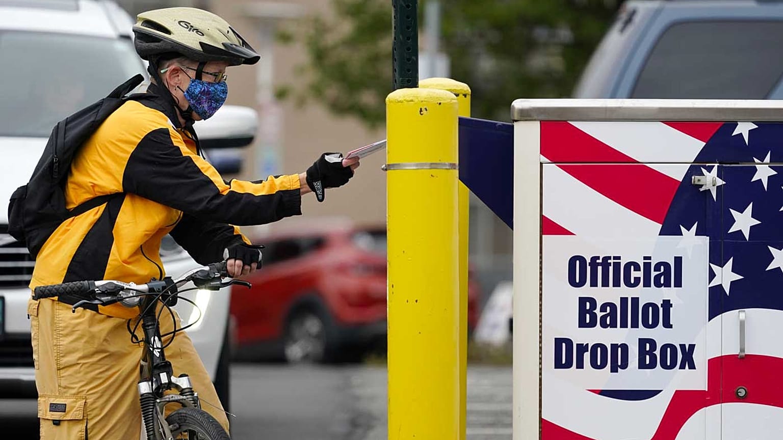 Il ciclista Mickey McDiarmid vota inserendo la scheda in un'urna elettorale per il voto postale lo scorso lunedì 19 ottobre 2020 a Bellingham, Washington