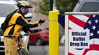 Il ciclista Mickey McDiarmid vota inserendo la scheda in un'urna elettorale per il voto postale lo scorso lunedì 19 ottobre 2020 a Bellingham, Washington