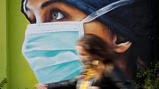 A woman walks in from of a mural painting of a nurse, in Milan, Italy, Wednesday, Oct. 14, 2020. 