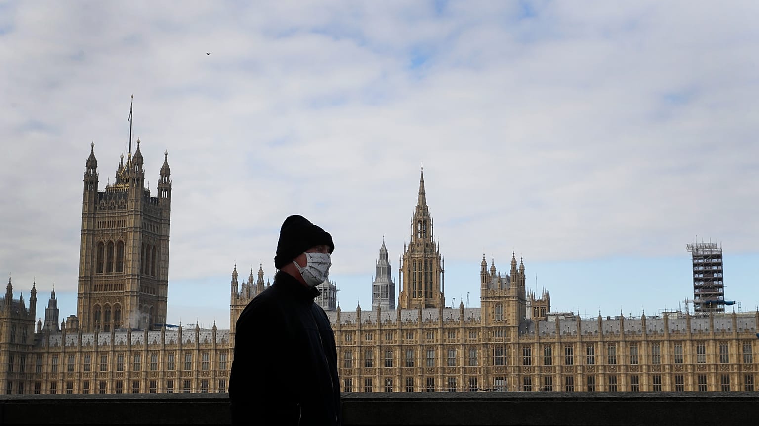 A man wears a face mask as he passes Britain's Parliament in London, Friday, Oct. 16, 2020. 