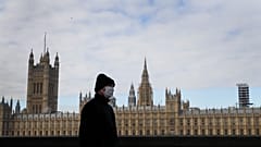 A man wears a face mask as he passes Britain's Parliament in London, Friday, Oct. 16, 2020. 