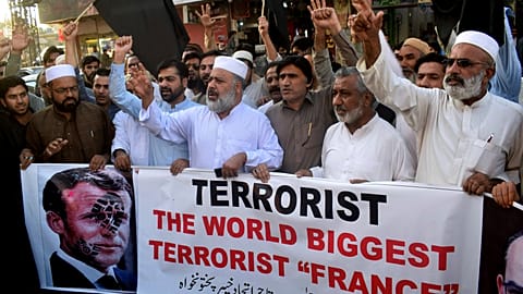 Pakistan traders hold a banner with a defaced picture of French President Emmanuel Macron during a protest against the publishing of caricatures of the Prophet Muhammad.