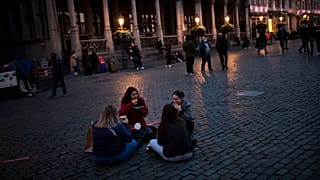 Students sit and eat waffles on Grand Place during an autumn evening prior to the curfew in downtown Brussels, Oct. 23, 2020.