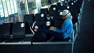 A passenger, wearing a face mask to protect against the spread of coronavirus, sits before boarding her flight at the Zaventem international airport