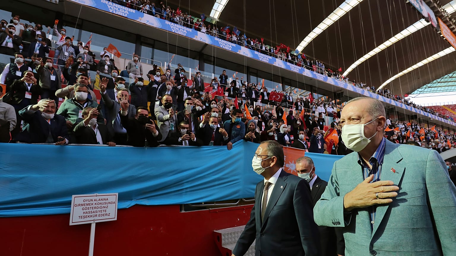 Turkey's President Recep Tayyip Erdogan, right, wearing a mask to help protect against the spread of coronavirus, greets his ruling party members gathered in a stadium, in Kay