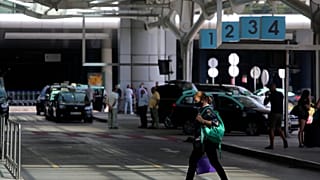 A woman wearing a face mask walks outside Lisbon's airport while in the background taxi drivers stand idle waiting for passengers, Friday, Sept. 11, 2020. Portugal