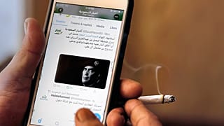 A man reads Saudi news on Twitter fronted by a picture of the prominent bodyguard to Saudi Arabia's King Salman Maj. Gen. Abdulaziz al-Fagham, at a coffee shop, in Jiddah