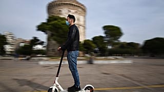 A man wearing a face mask against the spread of the coronavirus, rides an electric scooter in front of the White Tower 