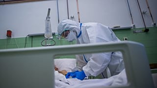 Ápoló védőfelszerelésben egy beteg pulzusát méri