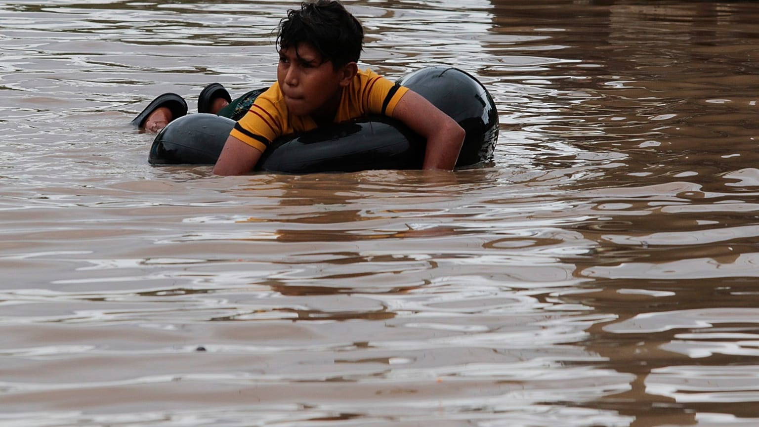 Un niño se tumba sobre un neumático hinchado en una calle inundada de Planeta, en Honduras