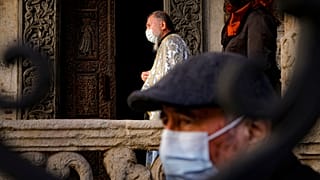 A priest wearing a mask for protection against the COVID-19 infection stands outside the Stavropoleos church, built in 1724, in Bucharest, Romania, Sunday, Nov. 8, 2020