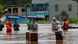 Hombres caminan por una calle inundada después del paso del huracán Iota en La Lima, Honduras