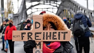 A woman attending a silent march against measures to curb the spread of coronavirus holds a cross reading "Freedom democracy" in Berlin on November 22, 2020.