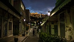 A woman walks on an empty street Plaka district of Athens with a part of the ancient Erechtheion temple on the Acropolis