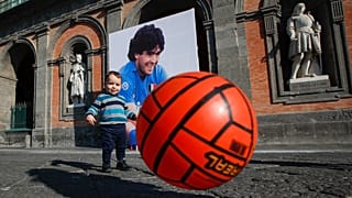 A child plays with a football in front of Naples' Royal Palace, which has a photo of Maradona hanging on it. Nov. 27, 2020.