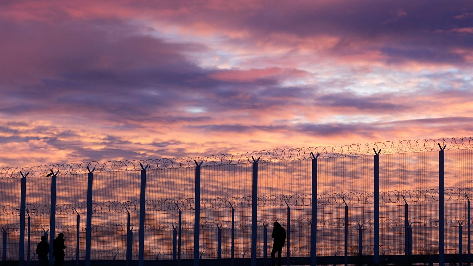 Migrants stand at a fence preventing them from reaching a highway beside the migrant camp known as the Jungle in Calais, northern France, Tuesday, Nov. 3, 2015