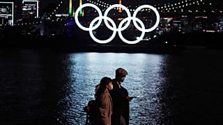 رجل وامرأة يمشيان حذو شعار الأولمبياد العائم في طوكيو. 2020/12/01