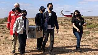 Miembros del Organismo de Exploración Aeroespacial de Japón cargan una caja que contiene muestras de asteroides que recuperaron en el sur de Australia tras su aterrizaje.