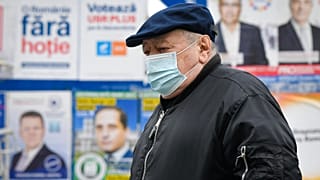 Un anciano con mascarilla camina junto a varios carteles electorales en Bucarest, la capital de Rumanía.
