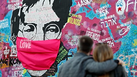  couple look at the Lennon Wall with a face mask attached to the image of John Lennon