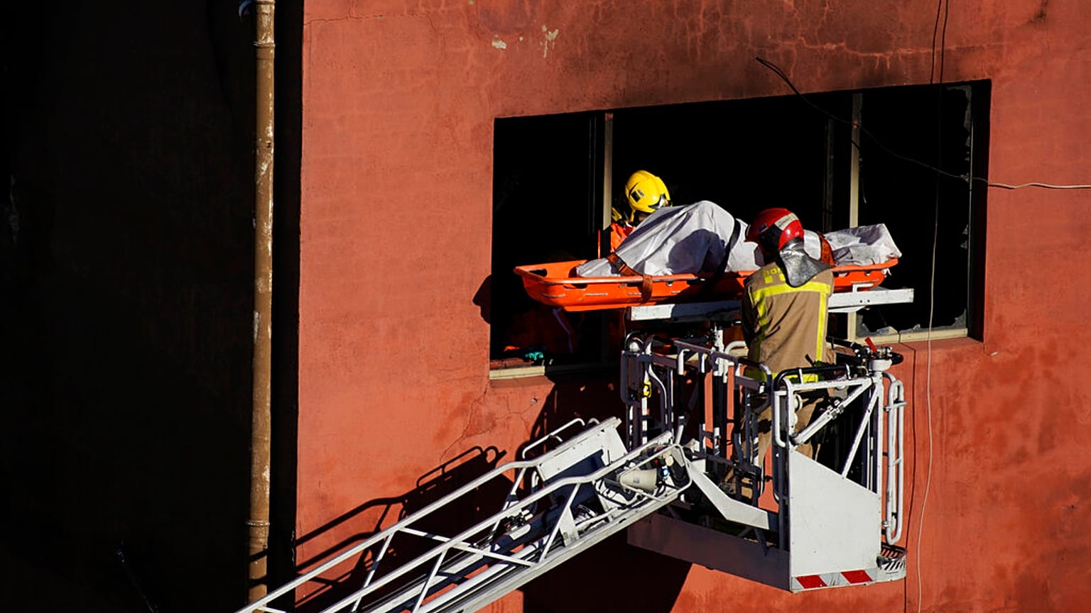 Firefighters load the body of a dead person into a crane after a fire on a building in Badalona, Barcelona, Spain, 