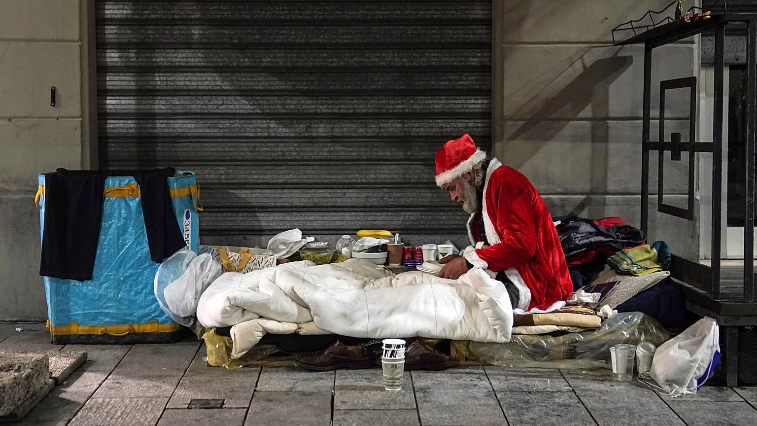 Un senzatetto, di nome Rafael, indossa un abito da Babbo Natale mentre si prepara a cenare sul ciglio di una strada, a Milano, giovedì 10 dicembre 2020